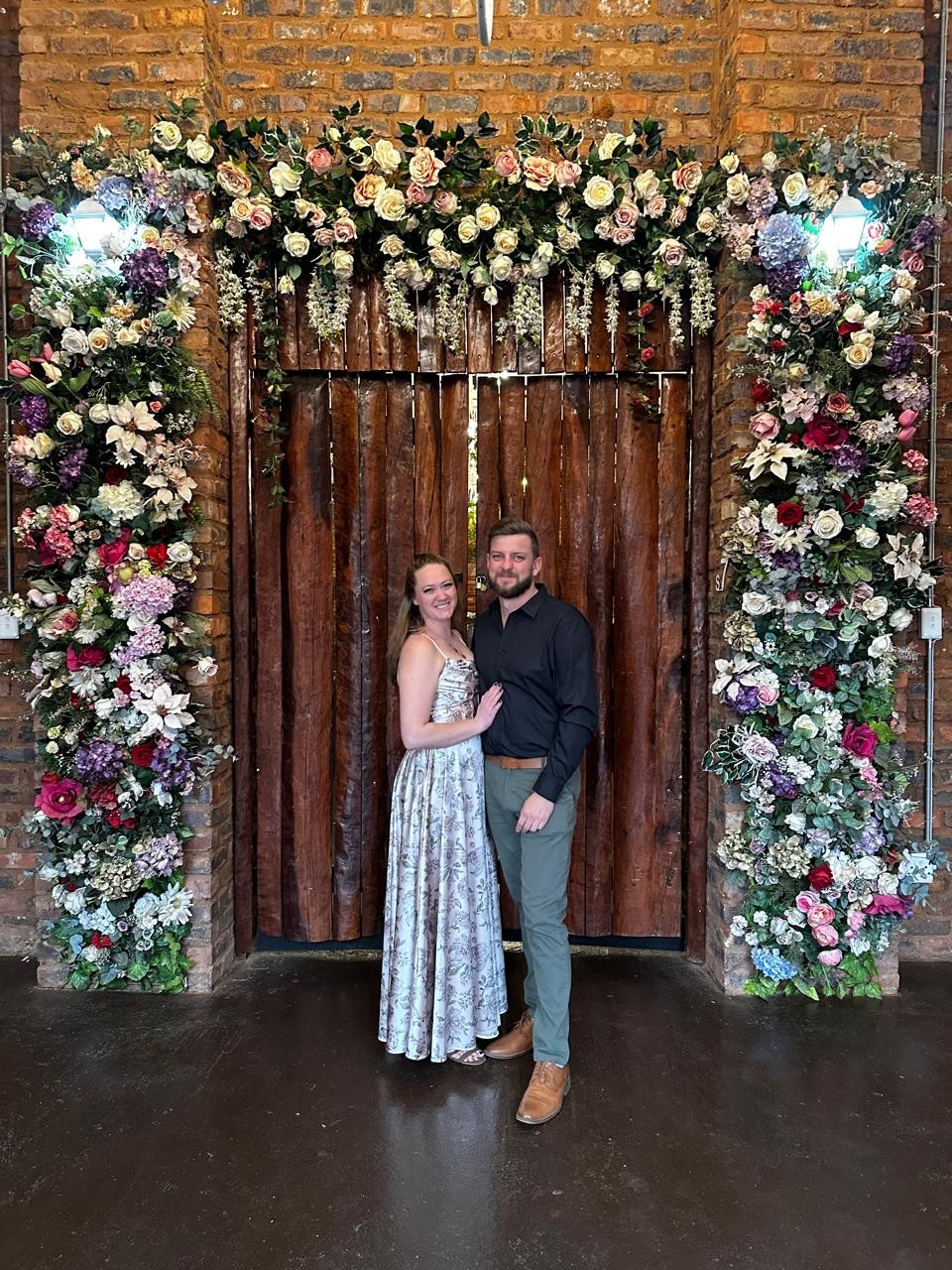 Amy and Andrew standing beneath an arch of flowers